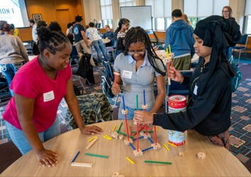 Three high school students work together to build a structure during a hands-on building exercise.